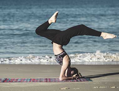 девушка занимается йогой и стоит в стойке на голове на берегу моря